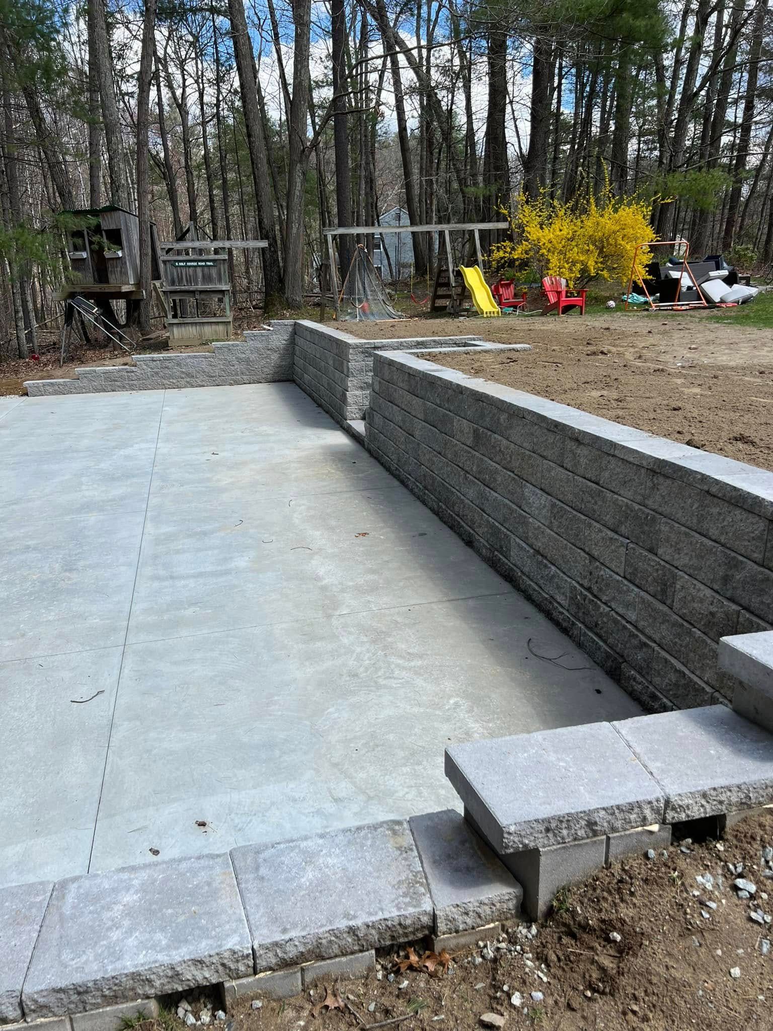 A concrete wall is being built in a backyard with trees in the background.