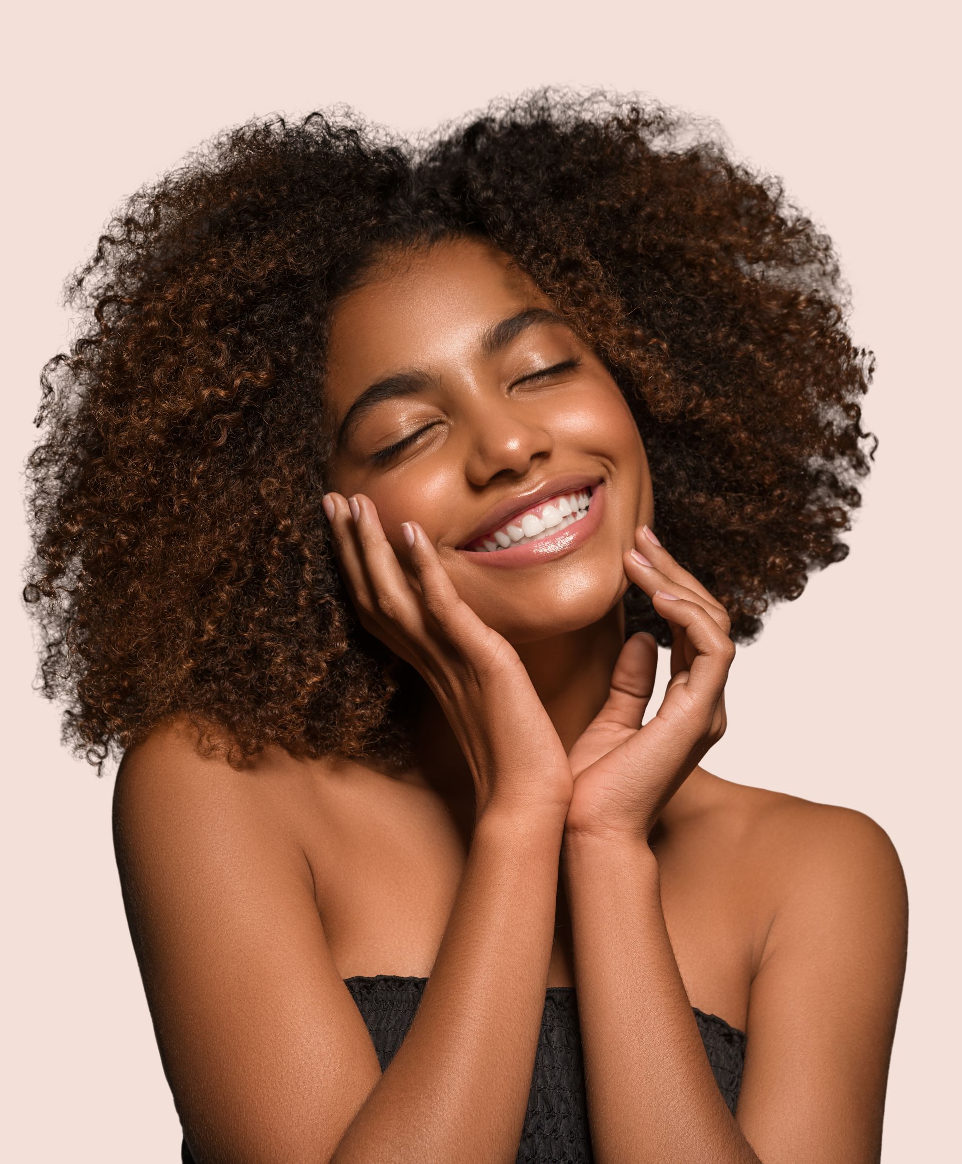 a woman with curly hair is smiling and touching her face with her hands .