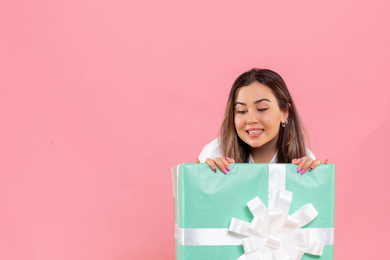 A woman is holding a green gift box with a white bow on a pink background.