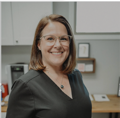 A woman wearing glasses and a black shirt is smiling for the camera.