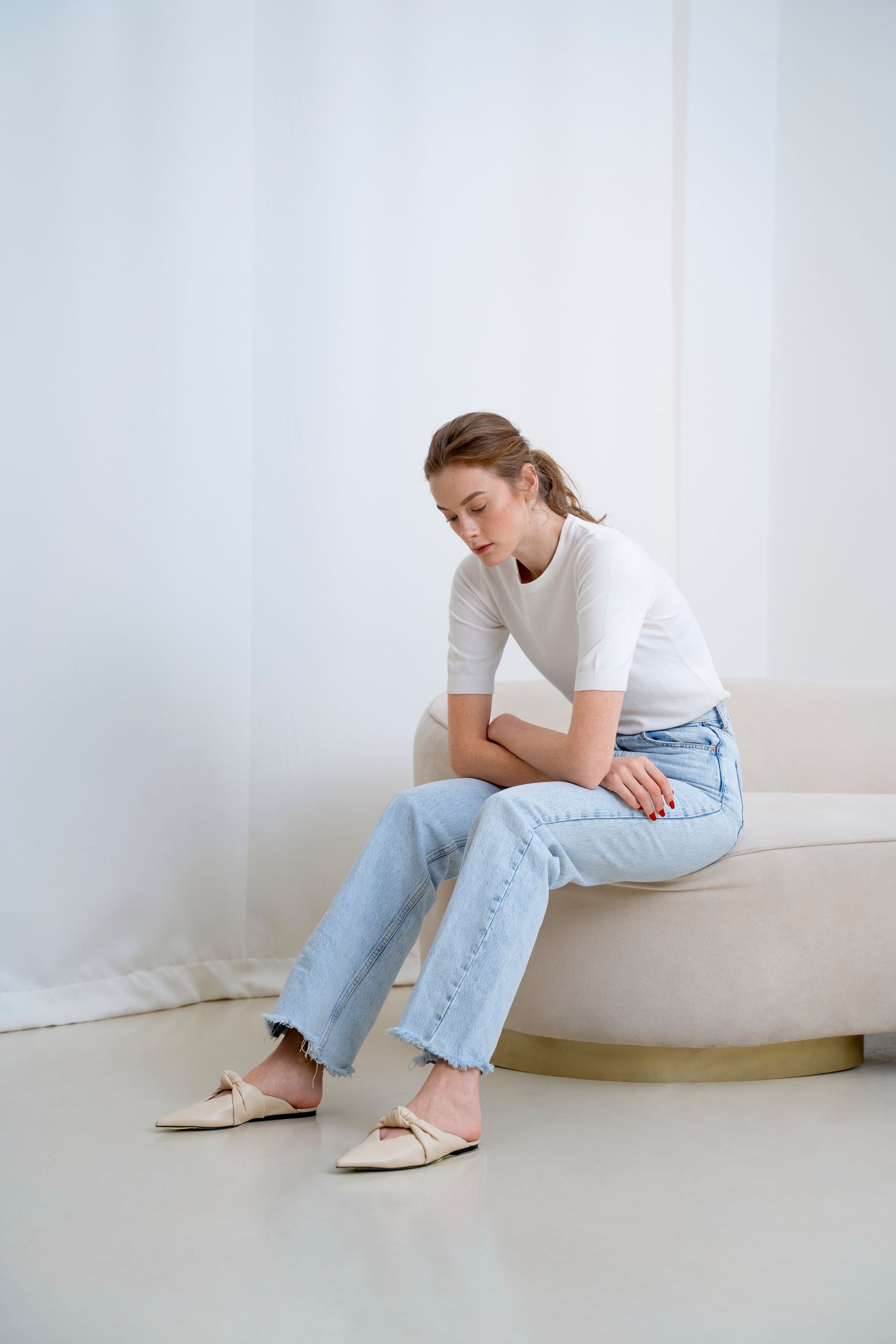 a woman is sitting on a couch wearing jeans and a white shirt .