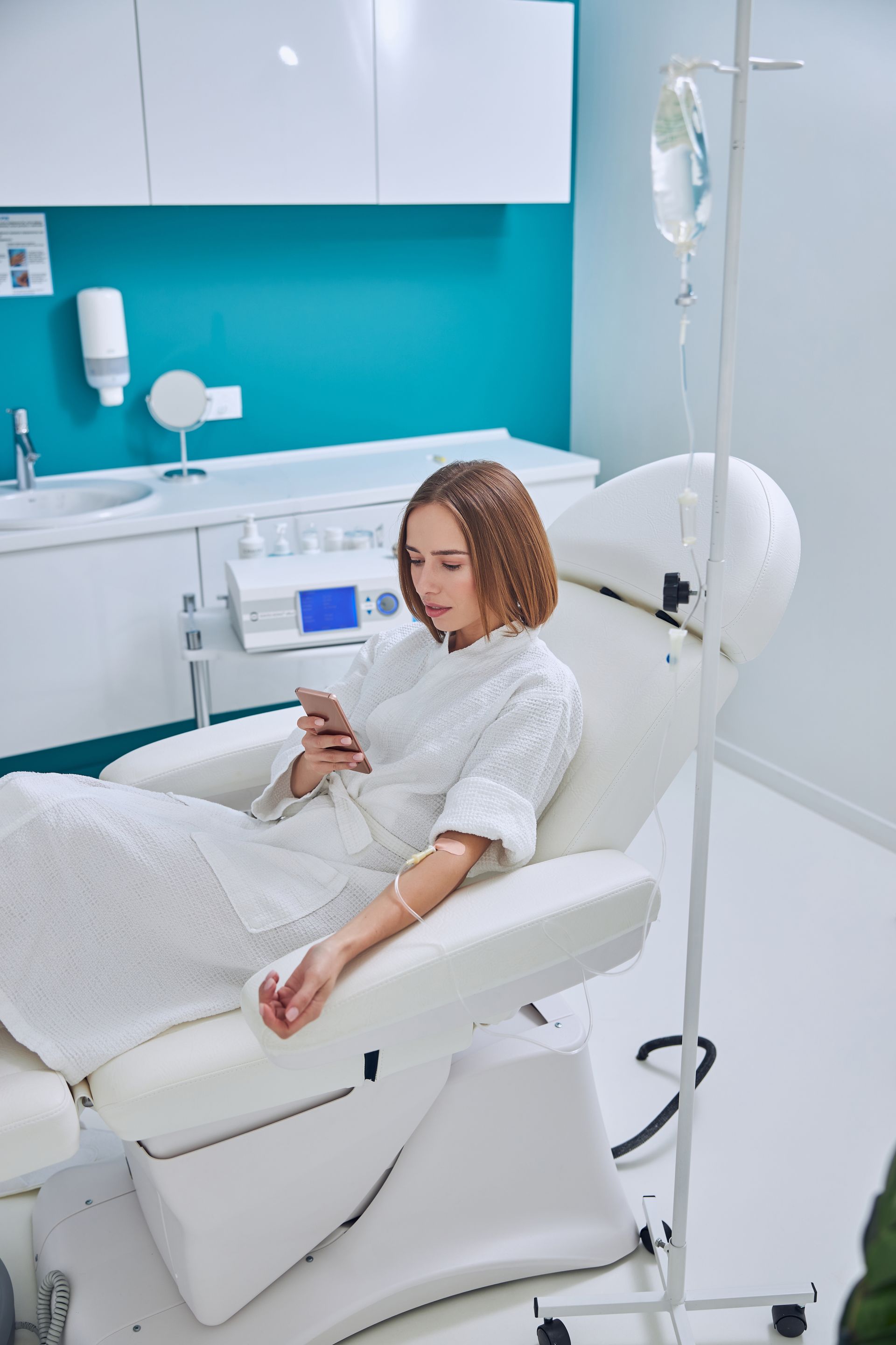 A woman is sitting in a chair with an iv in her arm and looking at her phone.