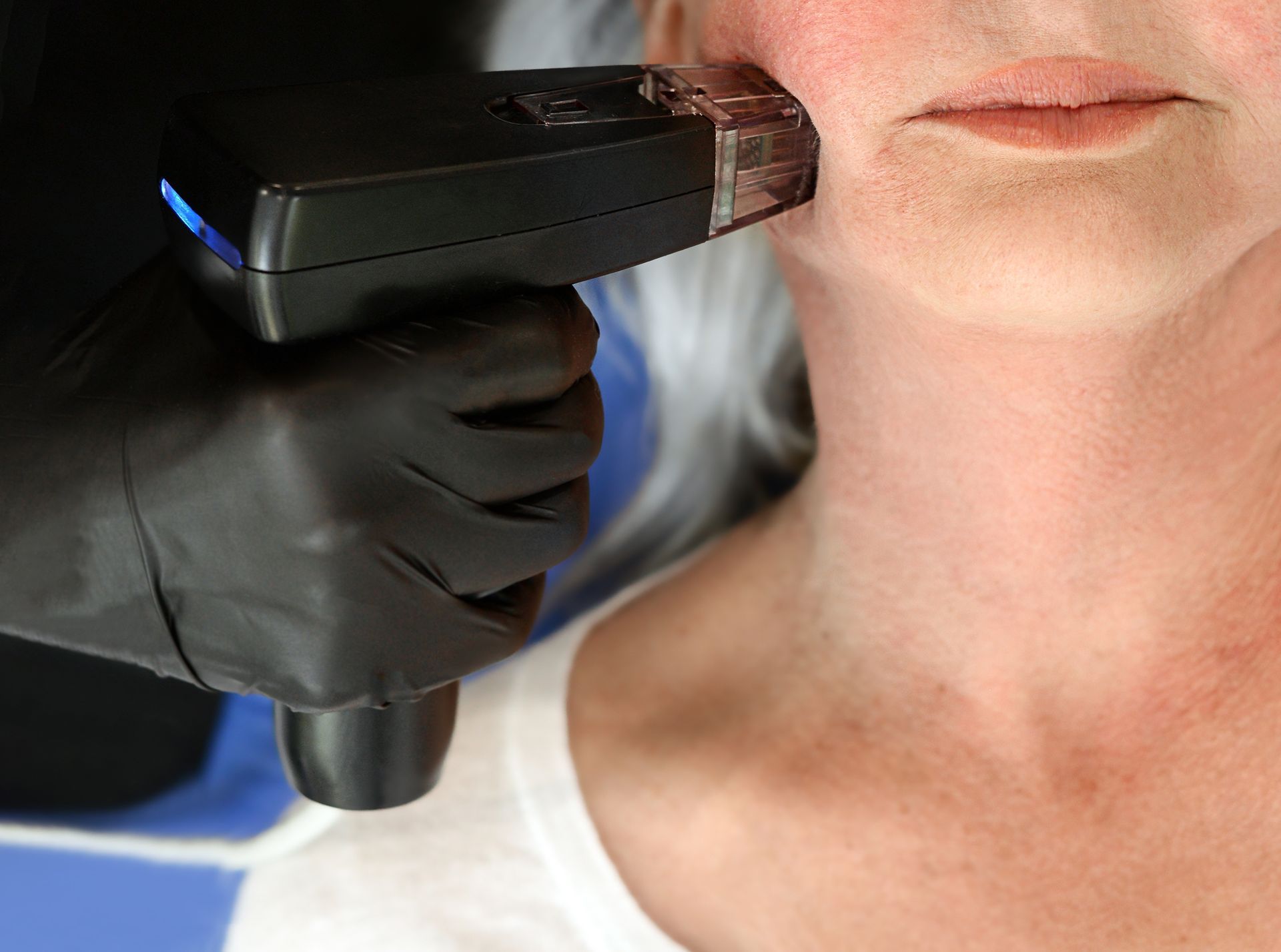 Gloved hand using a black handheld scanner near a woman’s jawline in a clinical setting