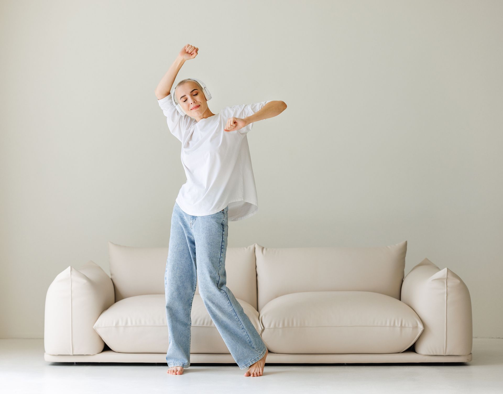 A woman is dancing in front of a white couch in a living room.