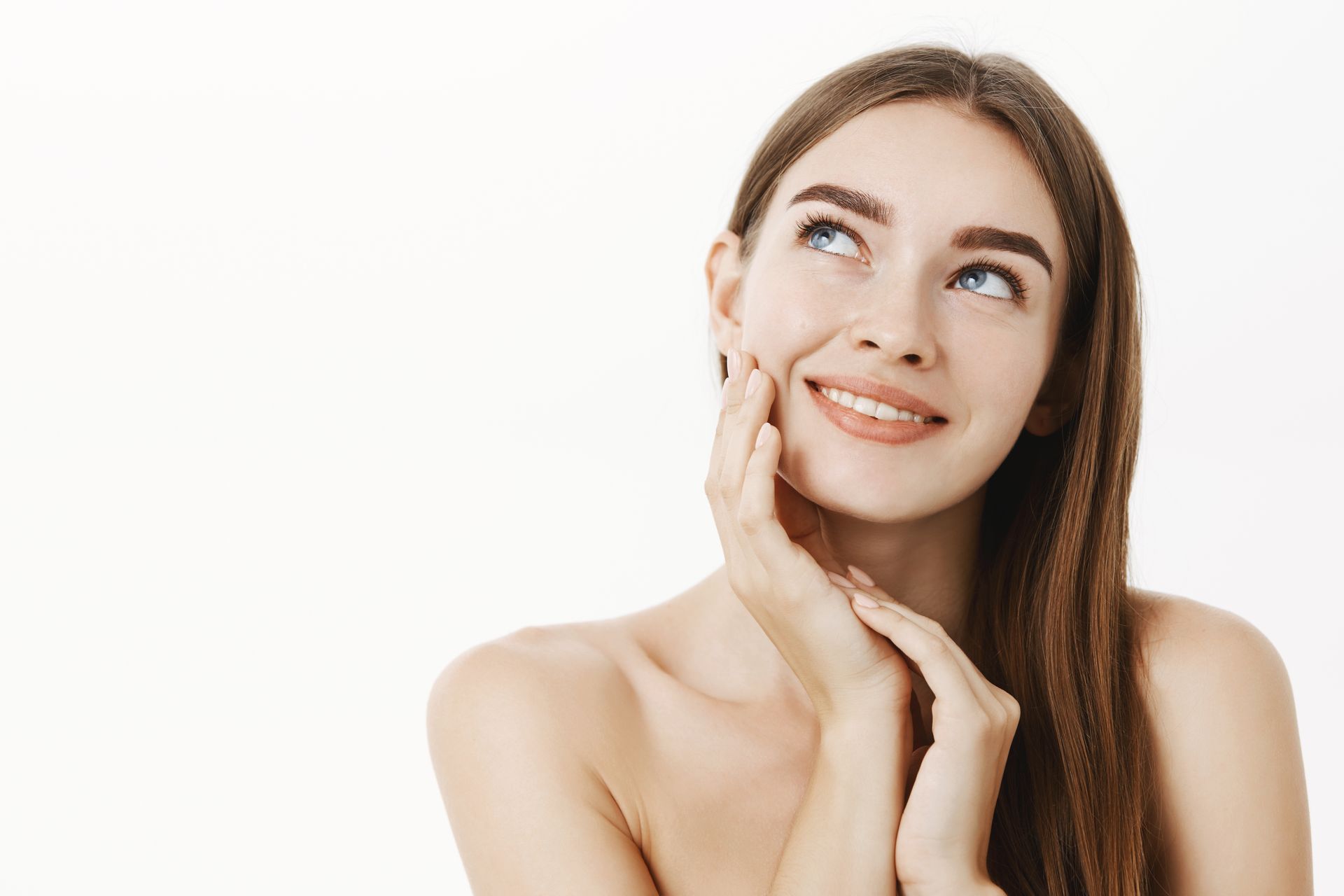 Smiling woman with long brown hair touching her face against a white background