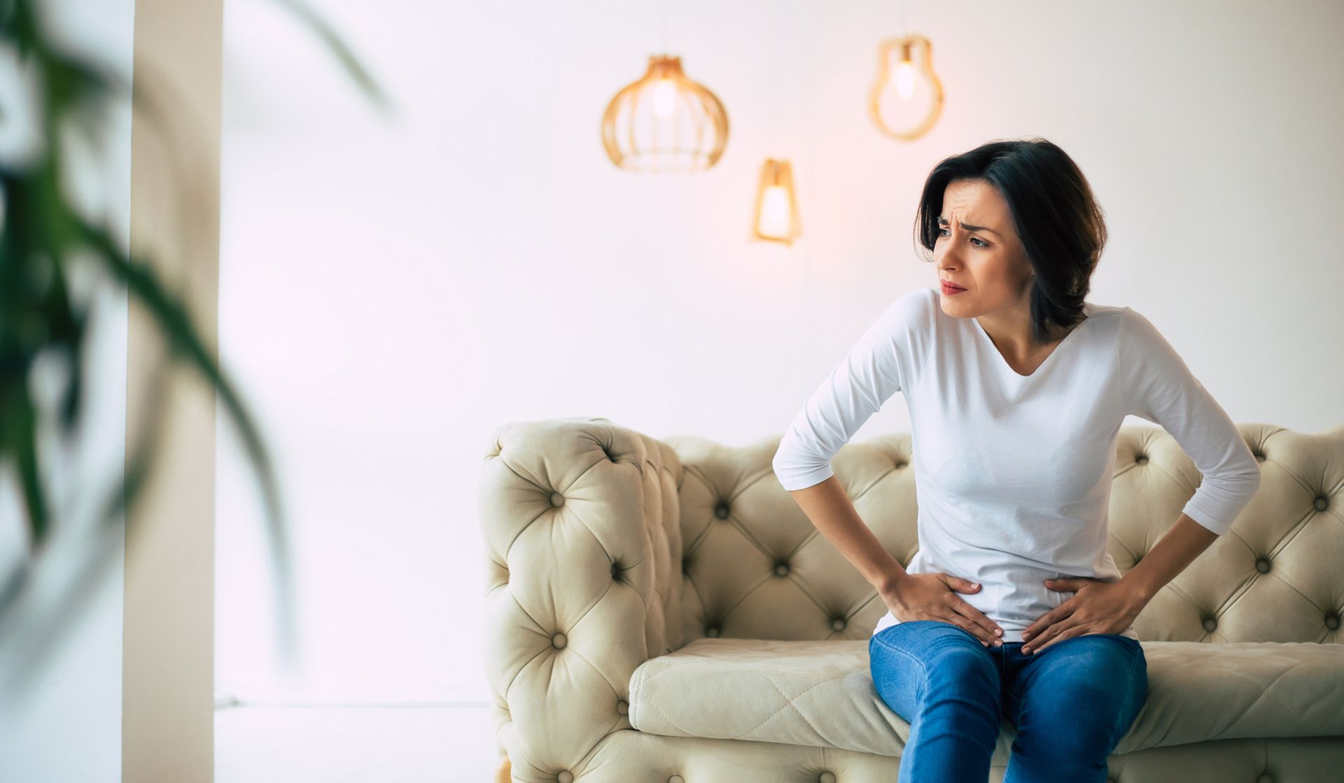 Woman on a couch holding her abdomen, appearing to be in pain, indoors.