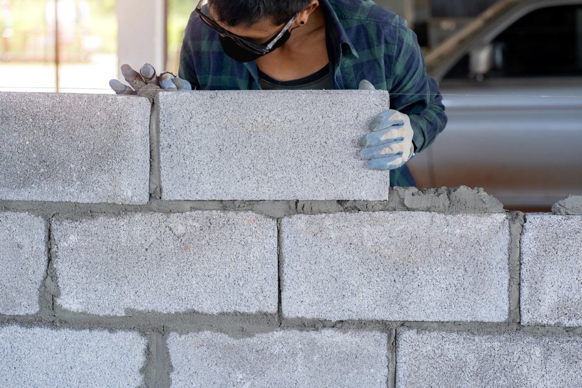 Person wearing safety glasses and gloves, laying concrete blocks with mortar.