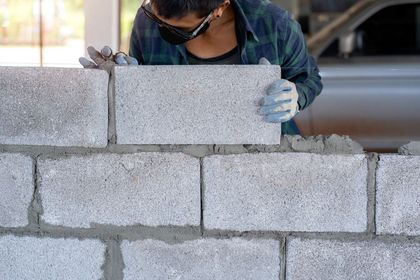 Person wearing safety glasses and gloves, laying concrete blocks with mortar.