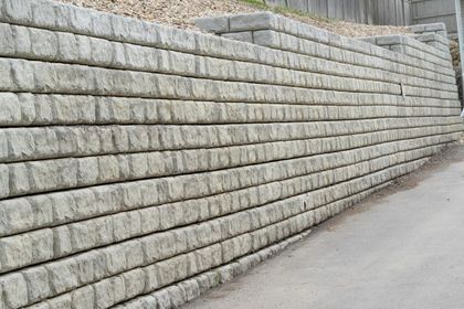 Gray retaining wall made of stacked concrete blocks alongside a road.