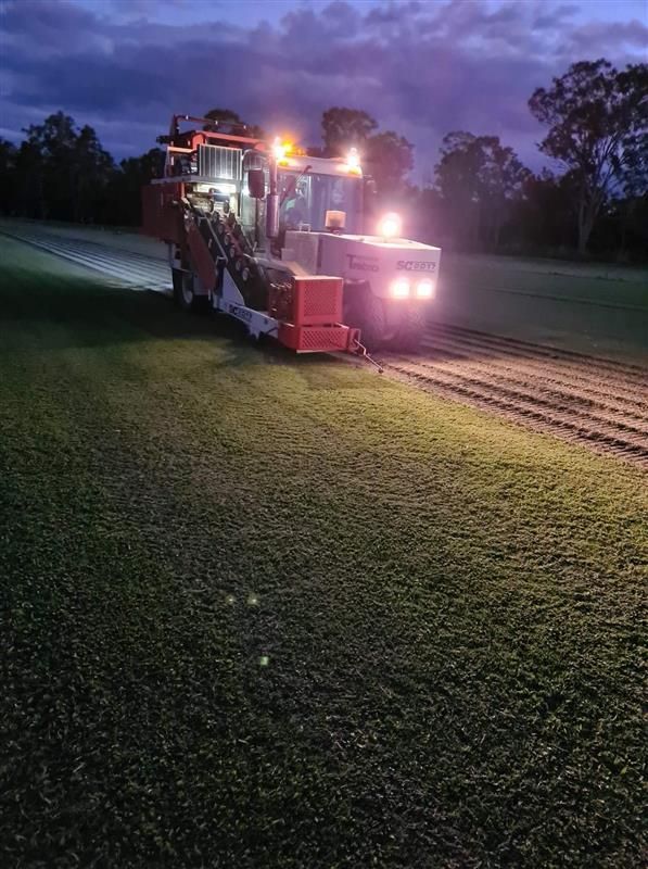 A Tractor Is Cutting Grass In A Field At Night — Barron River Lawns In Biboohra, QLD