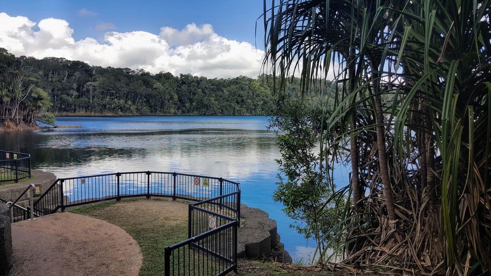 A Lake With A Fence Around It And Trees In The Background — Barron River Lawns In Yungaburra, QLD