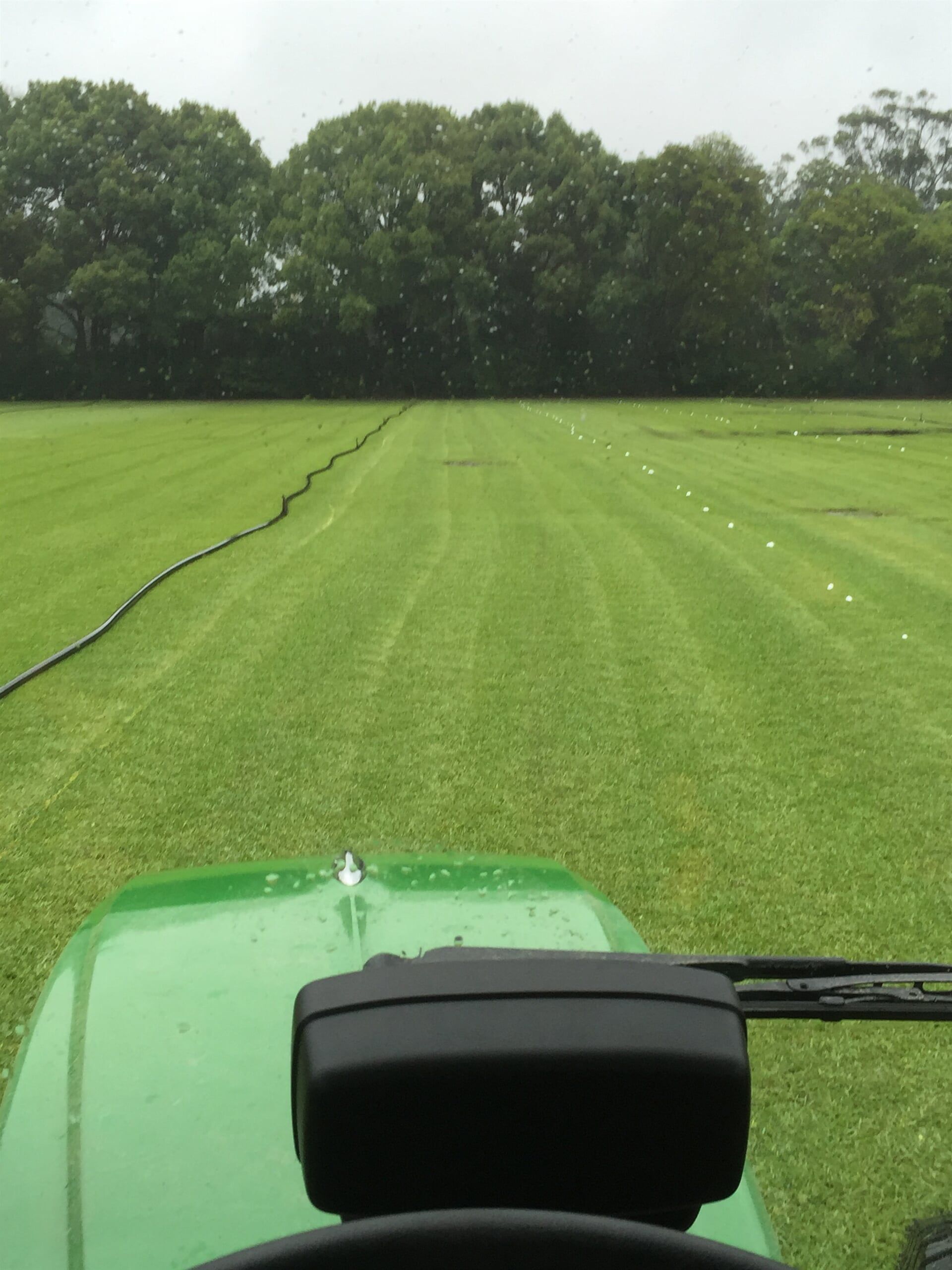 A Green Tractor is Driving Through a Grassy Field — Boambee Turf In Bonville, QLD