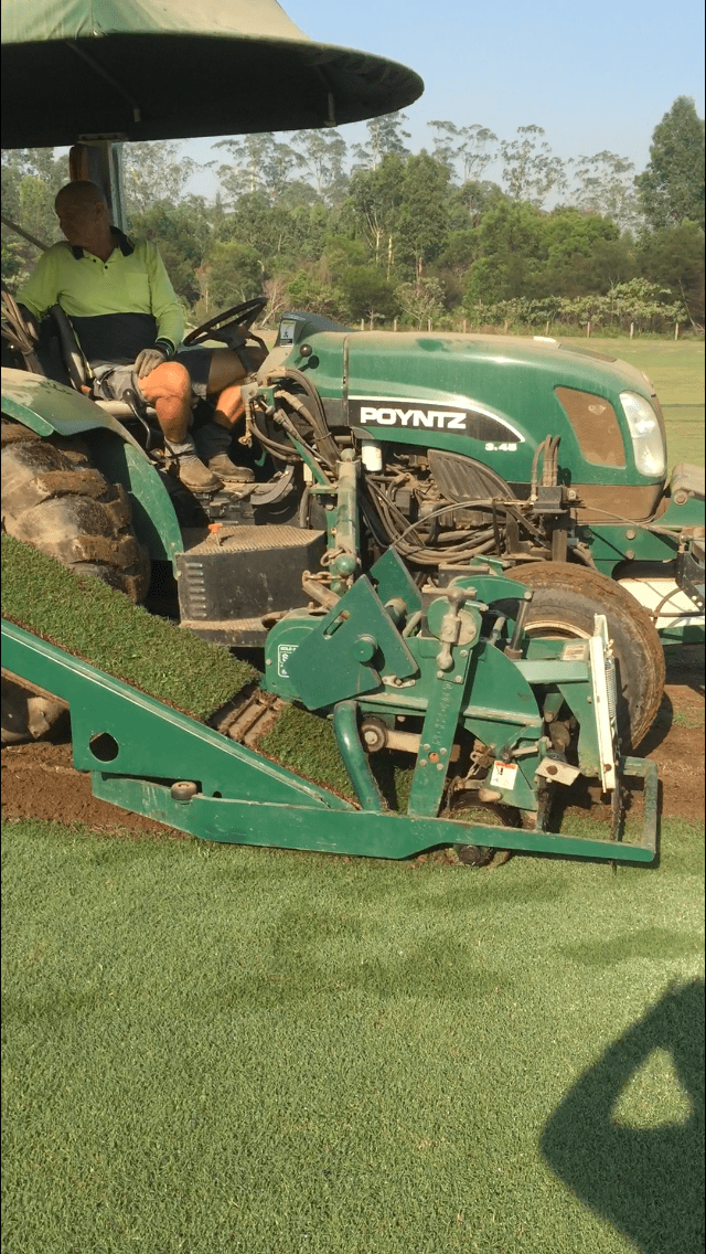 A Man is Driving a Green Tractor on a lush Green Field — Boambee Turf In Bonville NSW