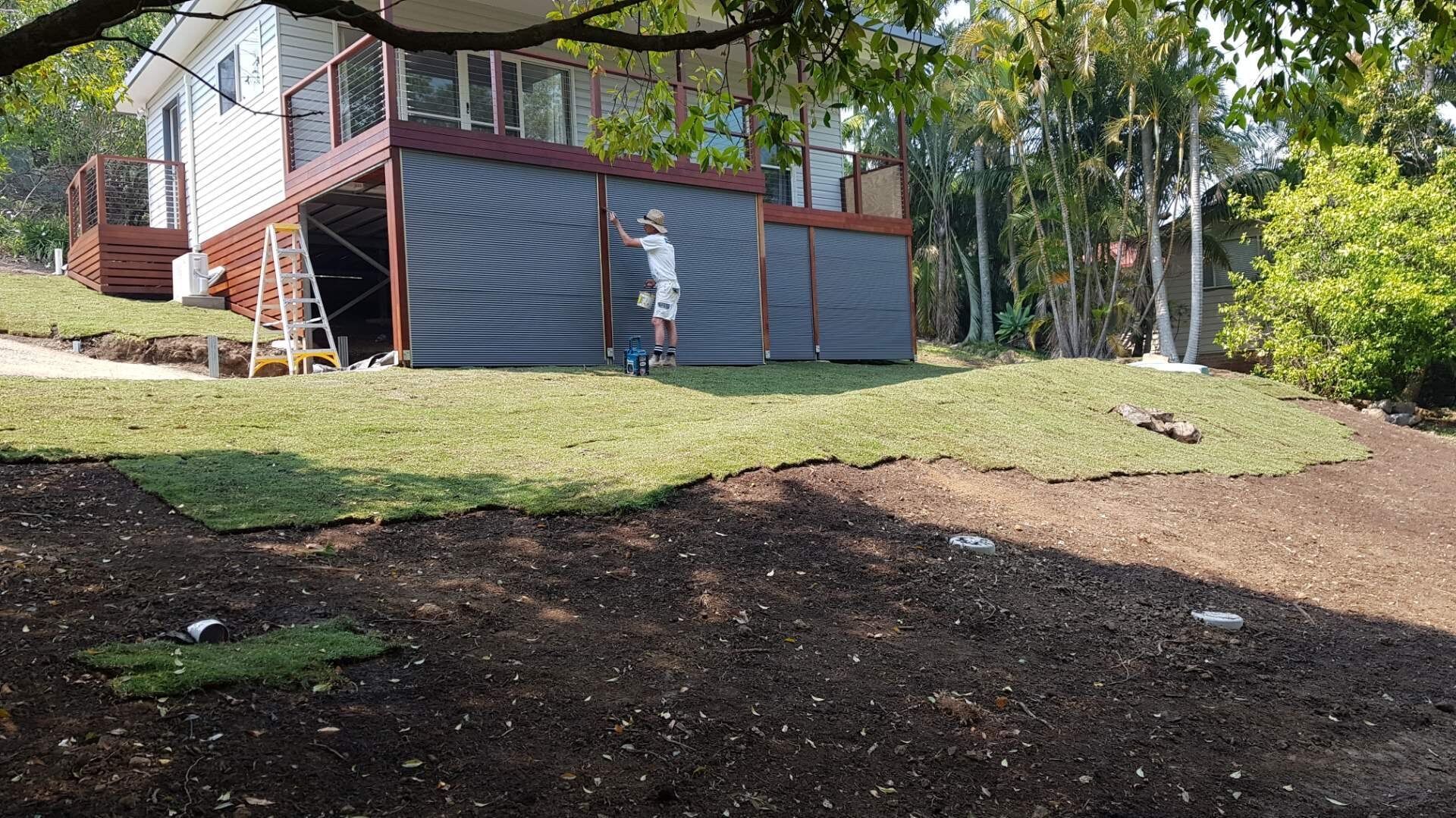 A Man is Standing on a Ladder in front of a House — Boambee Turf In Bonville, NSW