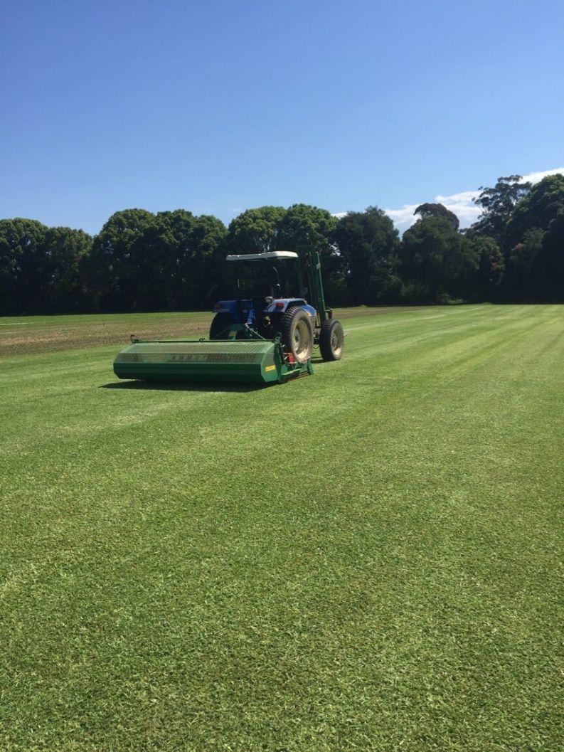 A Tractor is Cutting Grass on a Lush Green Field — Boambee Turf In Bonville, NSW