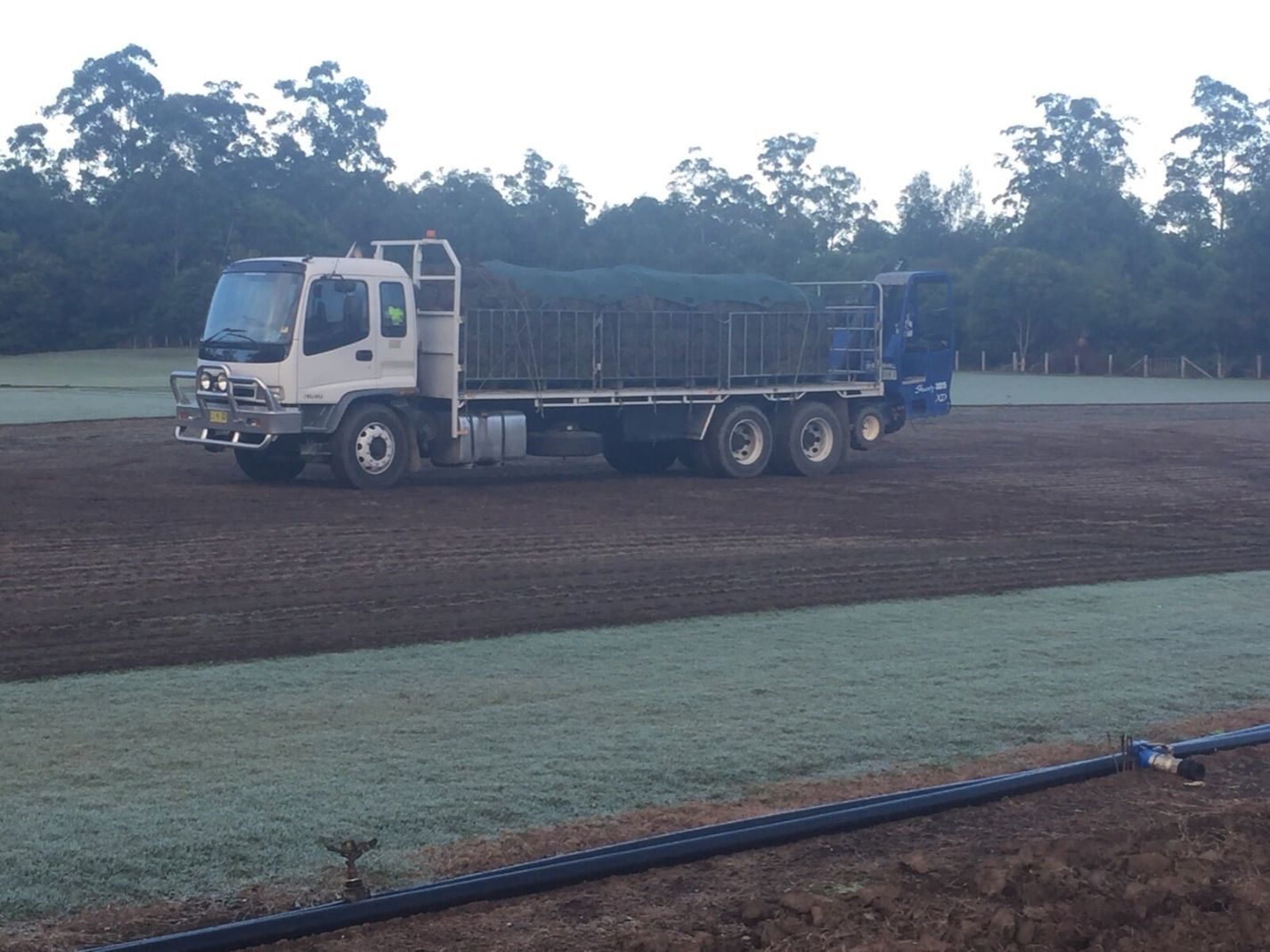 A White Truck is Parked in a field with trees in the Background — Boambee Turf In Bonville, NSW