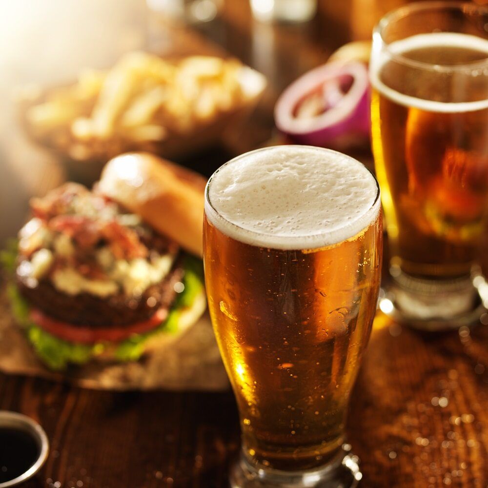 A Glass of Beer Sits on a Table Next to a Hamburger and French Fries — Capricorn Tavern in Taranganba, QLD