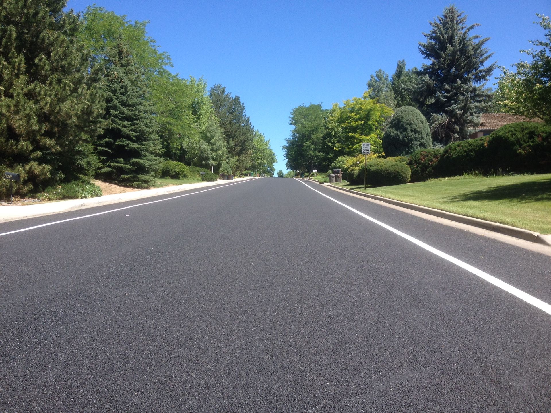 Construction worker applying sealant to asphalt, wearing safety gear: helmet, face shield, orange vest.