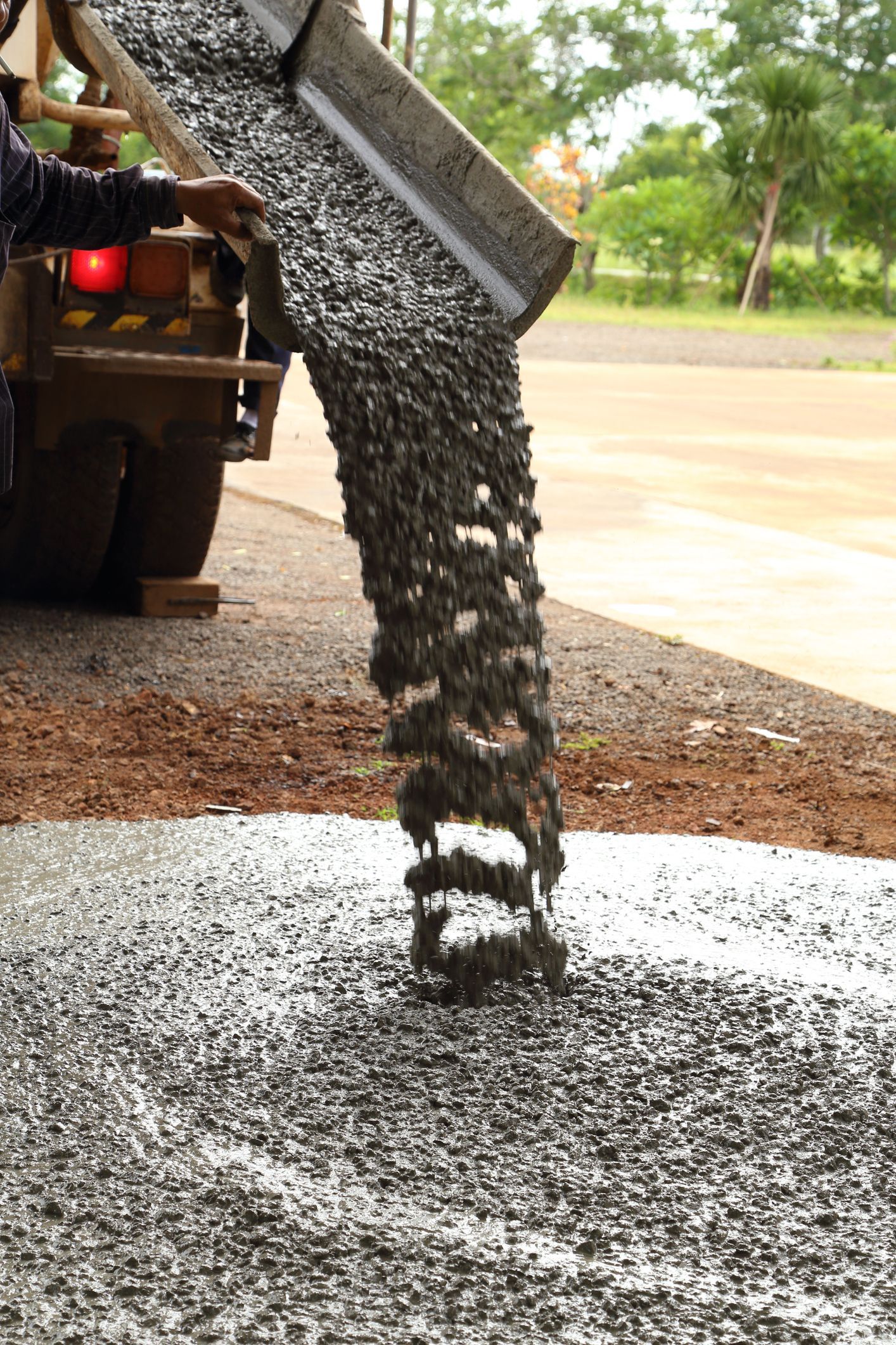 Truck pours cement on top of ground on bare sidewalk, with the forest in the background.