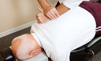A therapist pressing his hands & forearm on a man's back