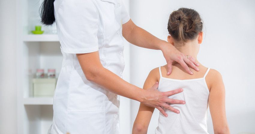 A child having her shoulders and back checked by a female therapist