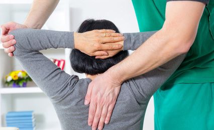 A therapist holding up a lady's arms so that he can check the movement in her shoulders and upper back