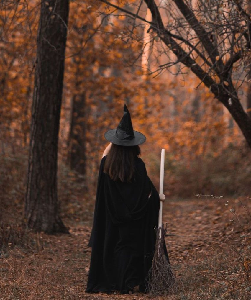a woman dressed as a witch is holding a broom in the woods .