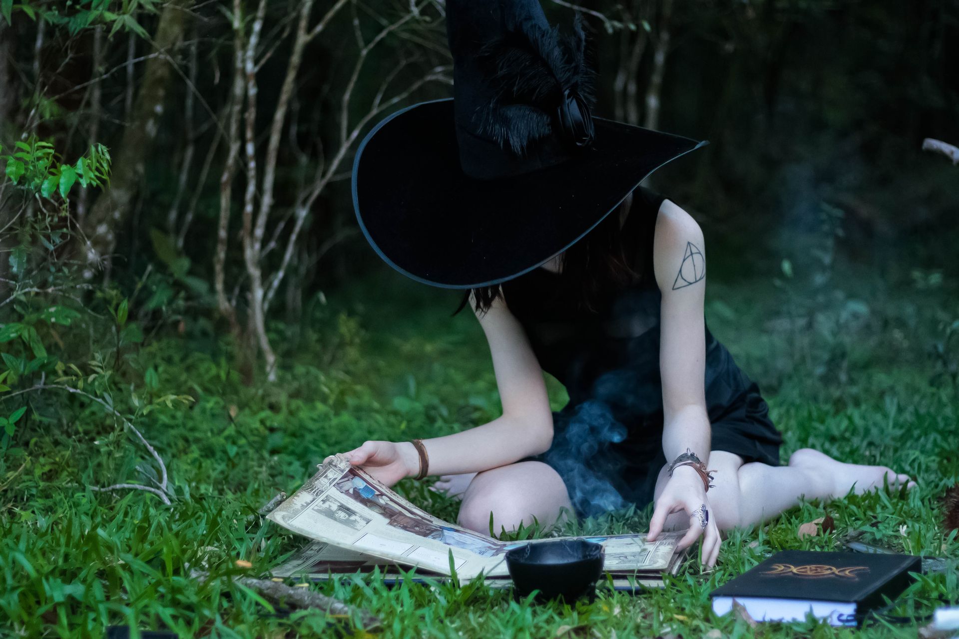 a witch in a hat is sitting on the grass reading a book.
