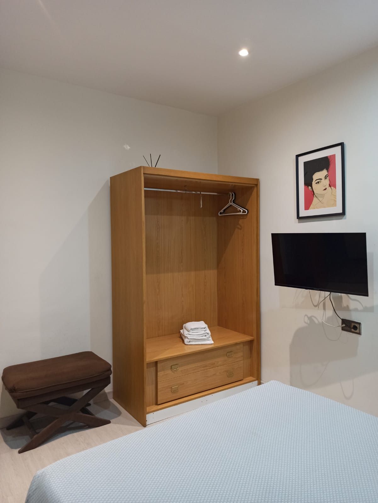 A bedroom with a bed , wardrobe , television and bench