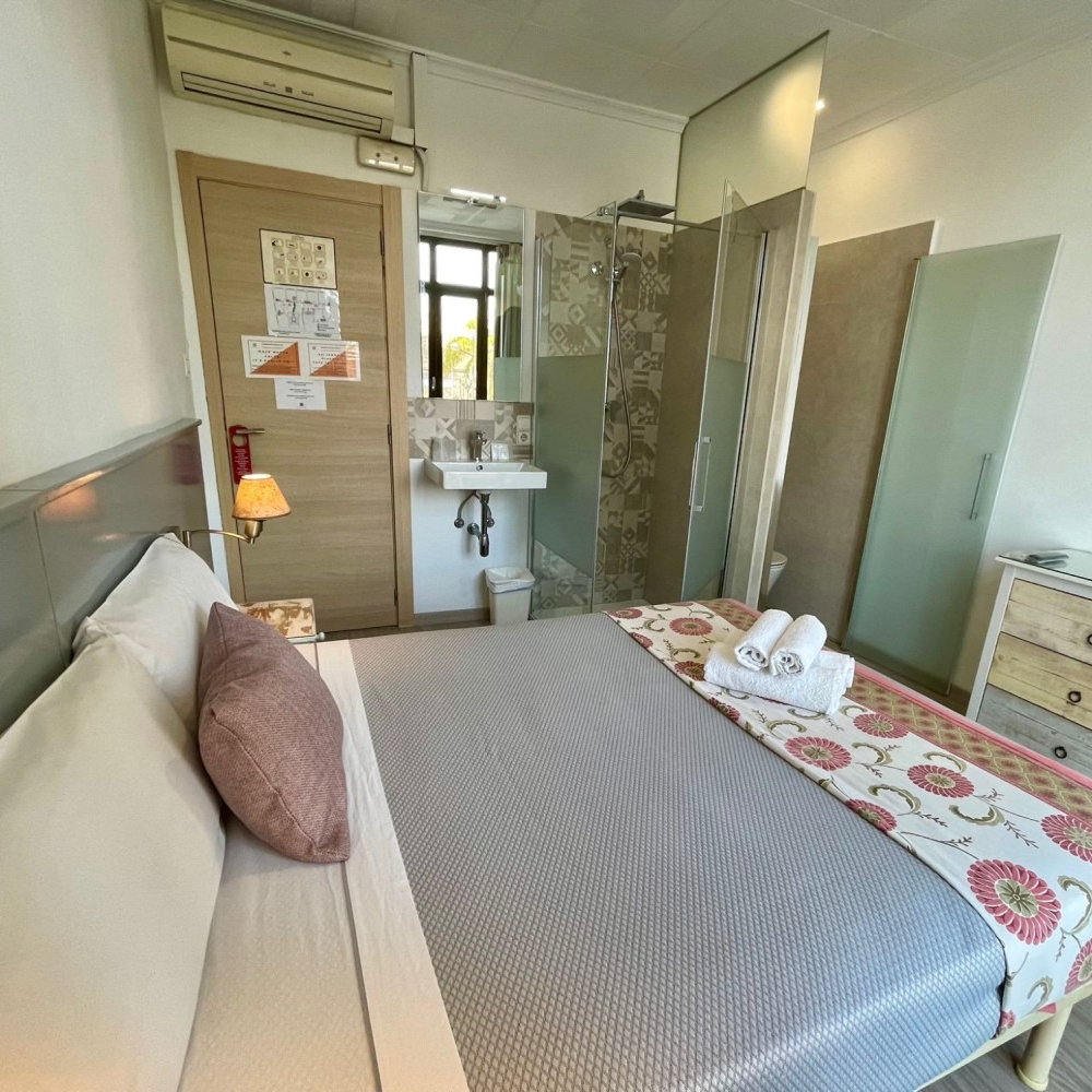 A bedroom with a bed , dresser , sink and shower.