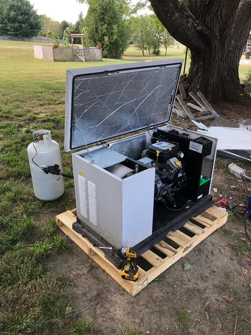 Outdoor portable industrial machine in an open case on a wooden pallet beside a large tree, with a gas tank nearby