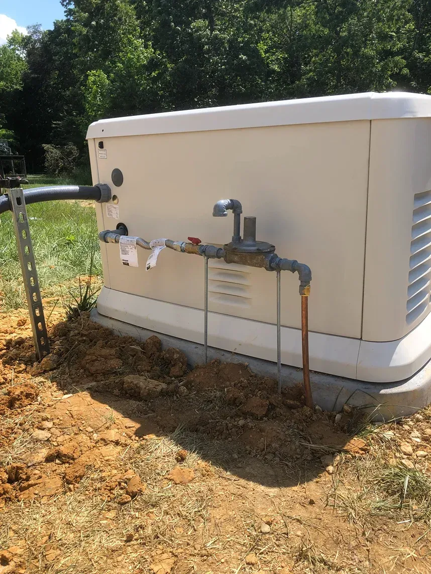 Outdoor utility equipment with white tank and metal piping on a dirt patch beside trees