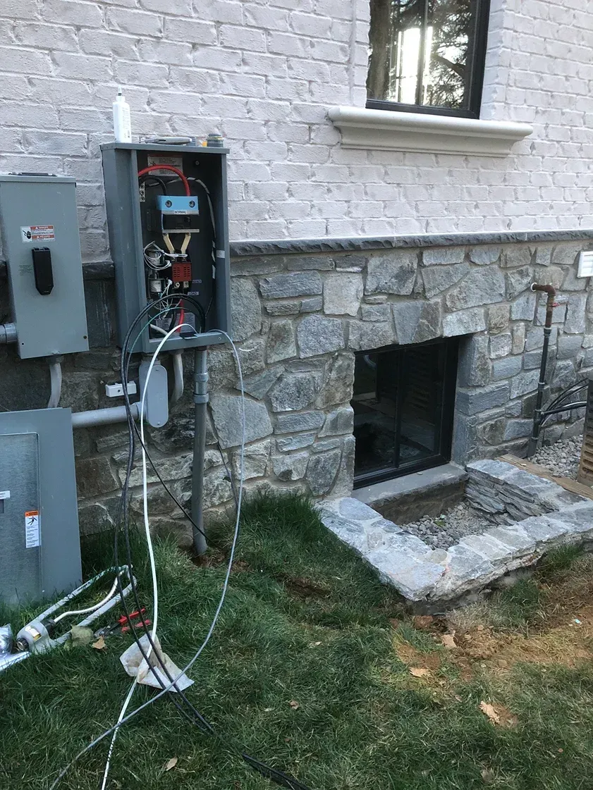 Stone house foundation with utility meters and an open basement window beneath a white wall