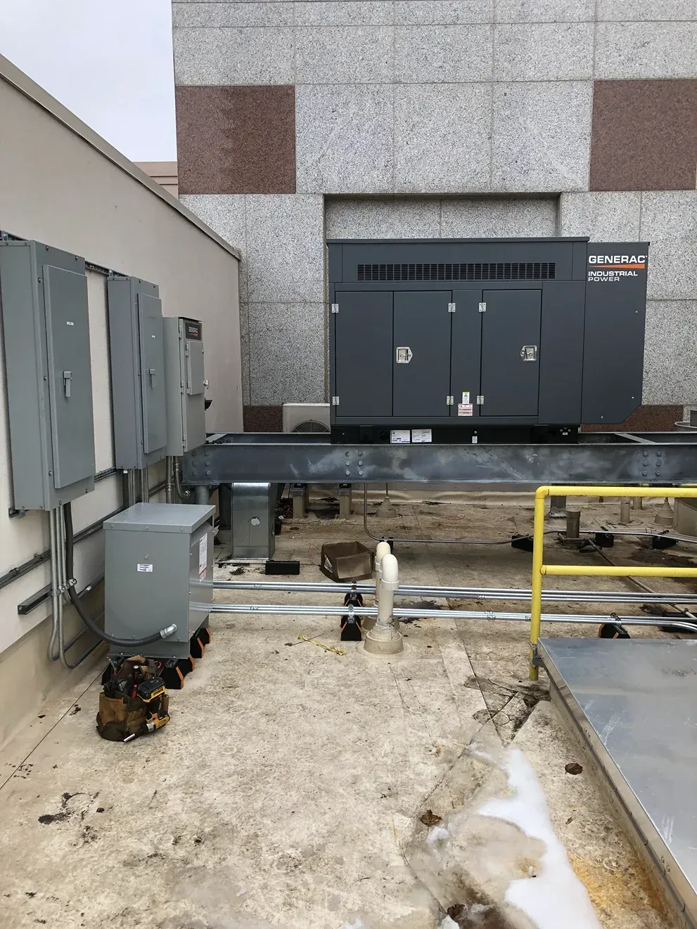 Outdoor industrial equipment on a rooftop, with gray HVAC units, pipes, and yellow safety railing.