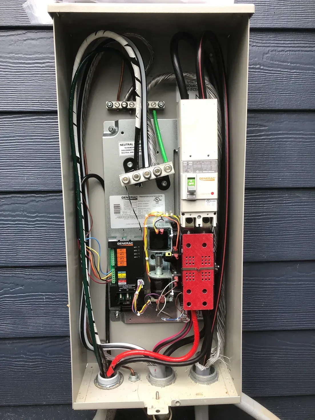 Open electrical control panel with wires, breakers, and red relay modules inside a gray outdoor enclosure