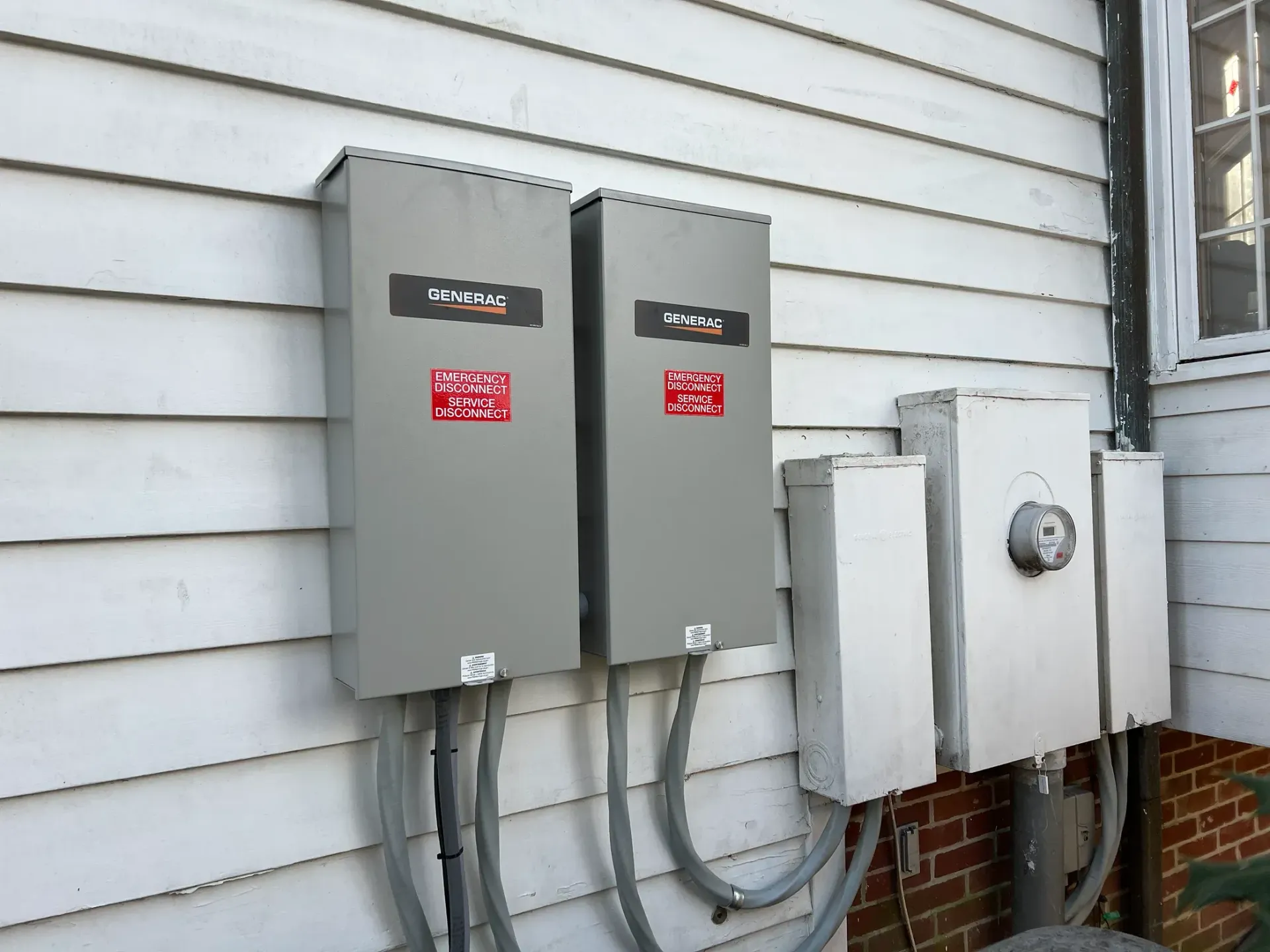 Three gray utility boxes and electrical meters mounted on a house exterior wall