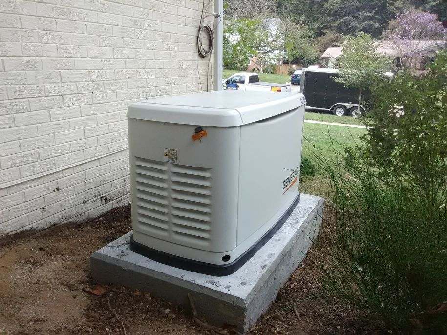 Outdoor standby generator on a concrete pad beside a house, with grass and parked cars in the background