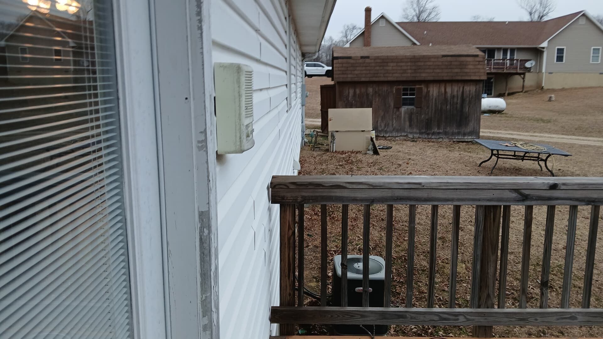 View from a house deck toward a backyard with a wooden shed, picnic table, and neighboring homes.