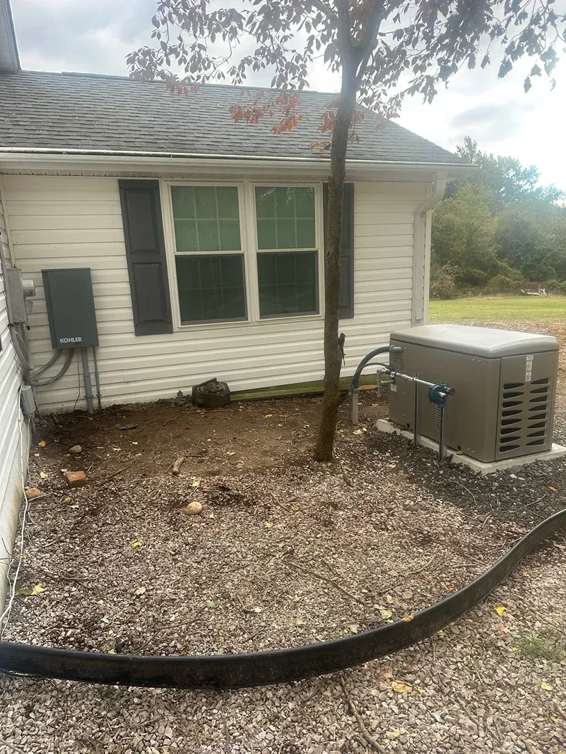 Side of a white house with green shutters, HVAC unit, and a tree in a mulched yard