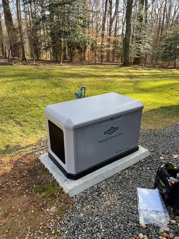 Gray outdoor generator on concrete pad in a grassy wooded yard