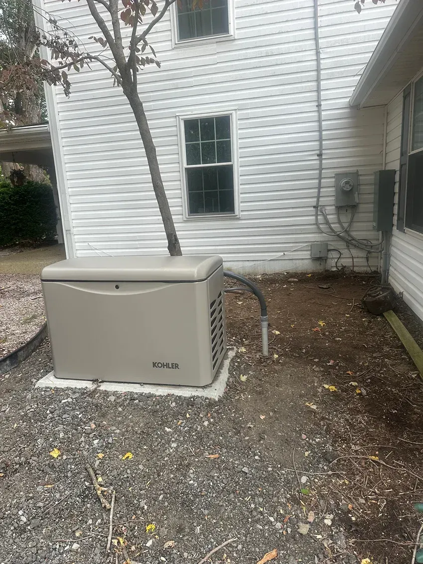 Outdoor generator beside a white house with gravel ground and an electrical meter on the wall