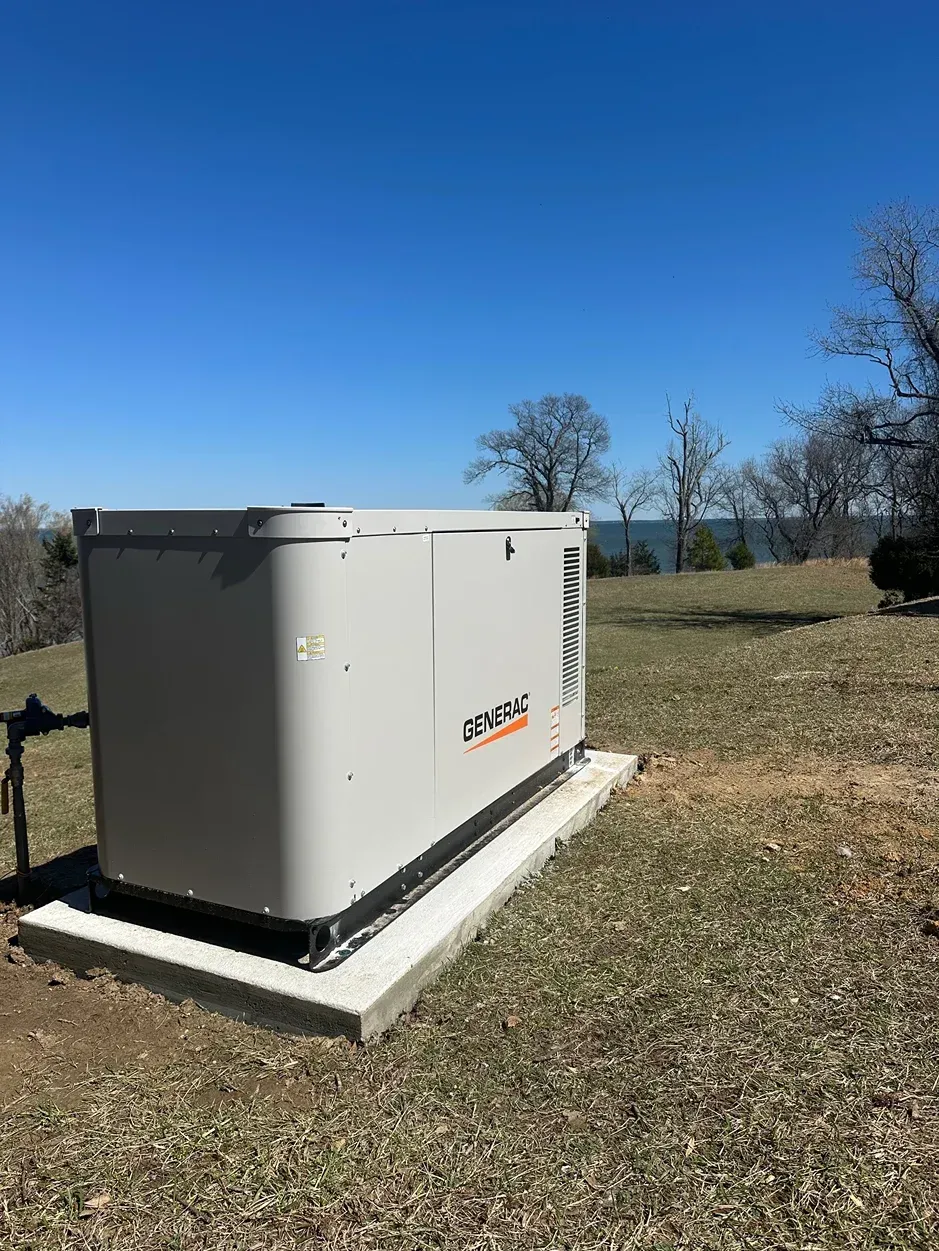 Gray generator on a concrete pad in a grassy field under a clear blue sky