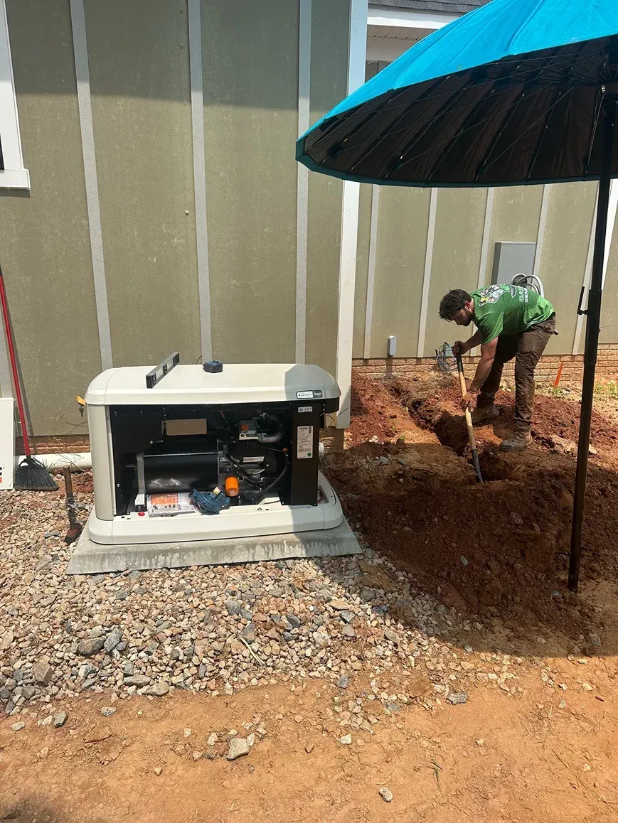 Generator beside a wall under a blue umbrella, with a person working in the background.