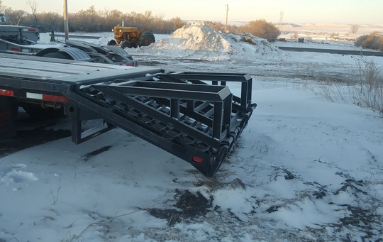 A trailer with a ramp attached to it is parked in the snow.
