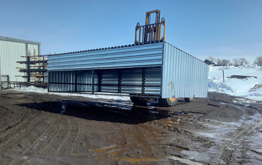 A large metal building is sitting in the middle of a dirt field.