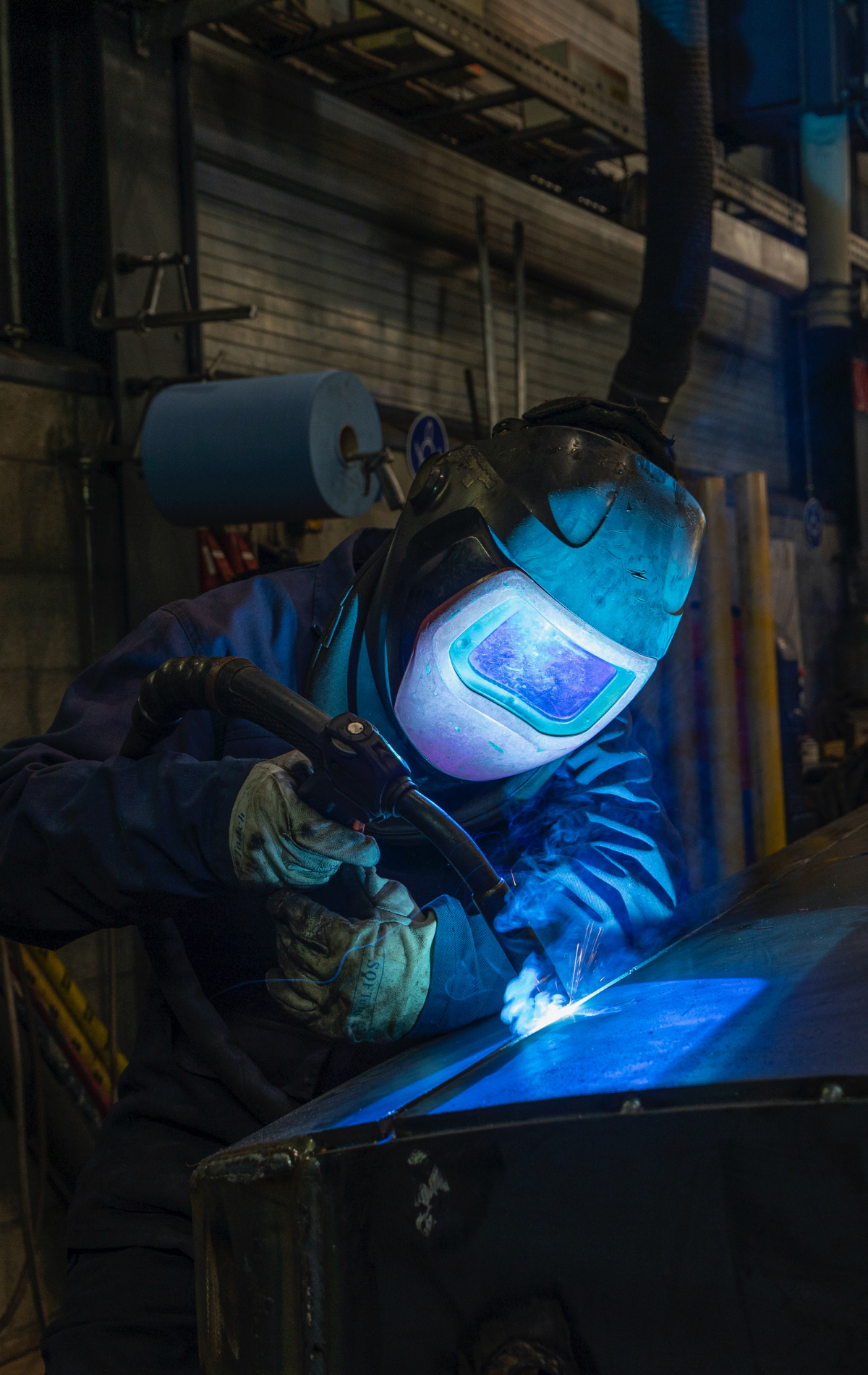 A man is welding a piece of metal in a factory.