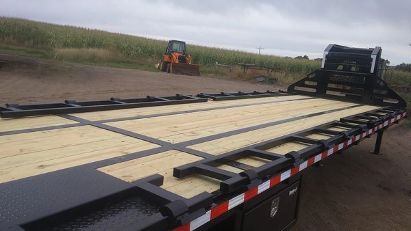 A trailer with a tractor in the background is sitting on a dirt road.