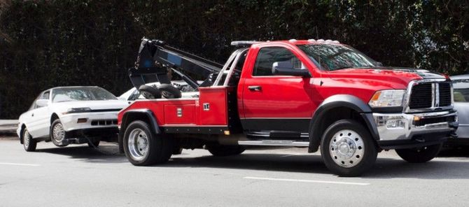 Red tow truck hauling a white sedan on a road