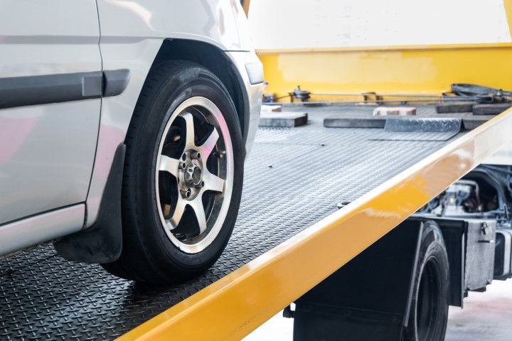 Silver car on a yellow tow truck ramp, close-up of the front wheel being loaded.