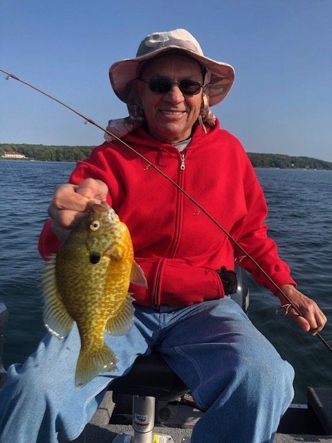 A man is sitting on a boat holding a fish and a fishing rod